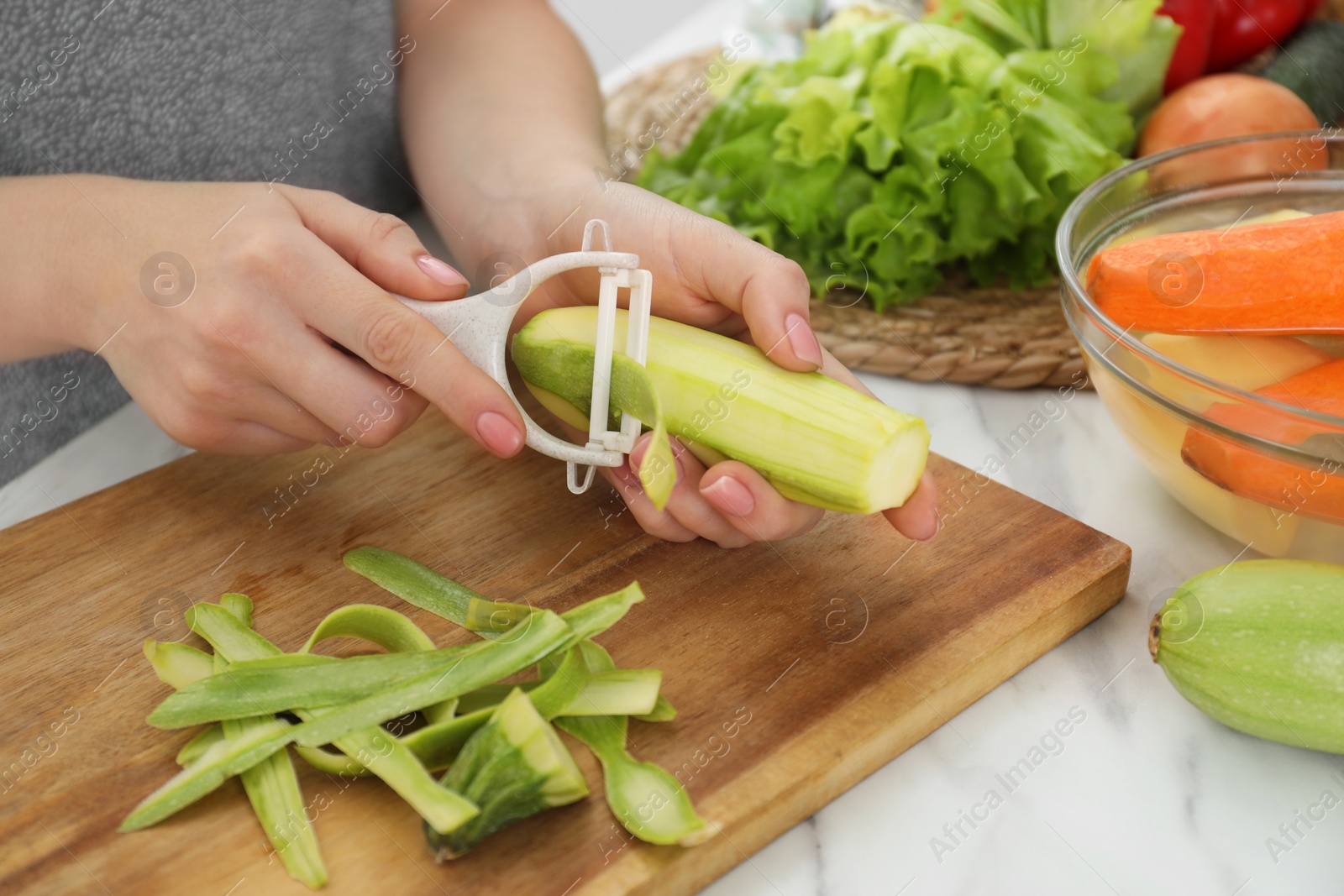 Photo of Woman peeling fresh zucchini at white marble table, closeup