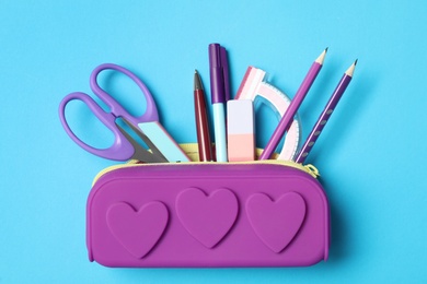 Photo of Pencil case with different stationery on light blue background, top view. Back to school
