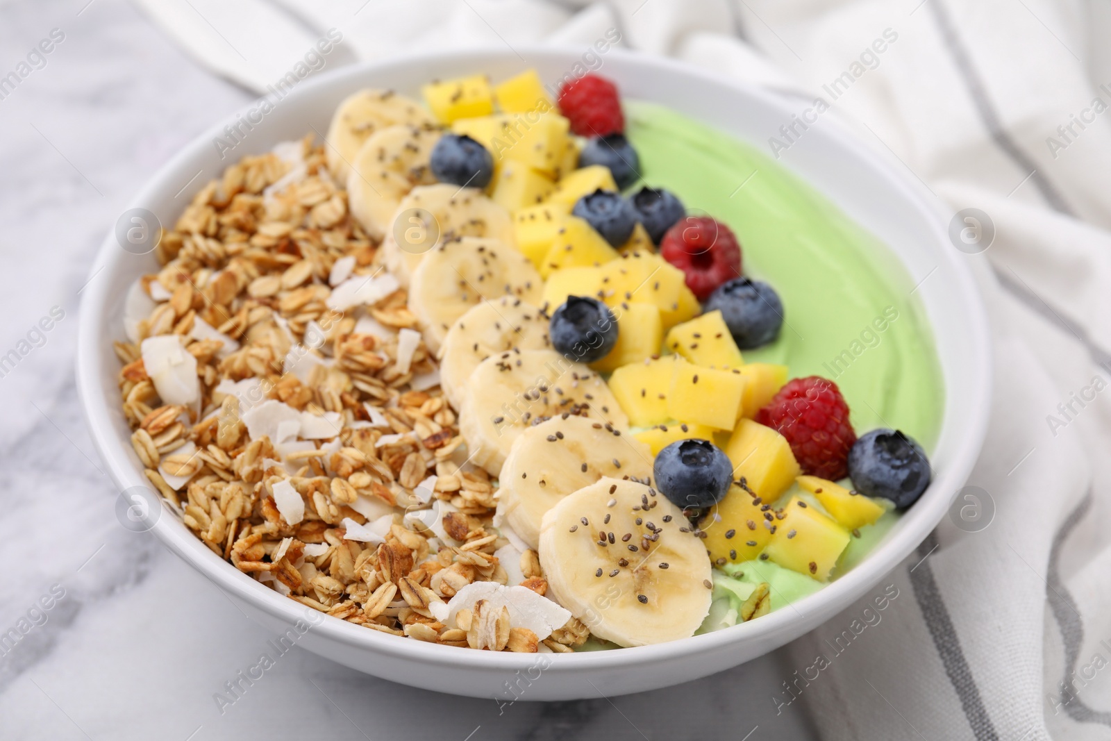 Photo of Tasty matcha smoothie bowl served with fresh fruits and oatmeal on white marble table, closeup. Healthy breakfast