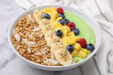 Photo of Tasty matcha smoothie bowl served with fresh fruits and oatmeal on white marble table, closeup. Healthy breakfast