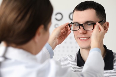 Photo of Vision testing. Ophthalmologist giving glasses to young man indoors