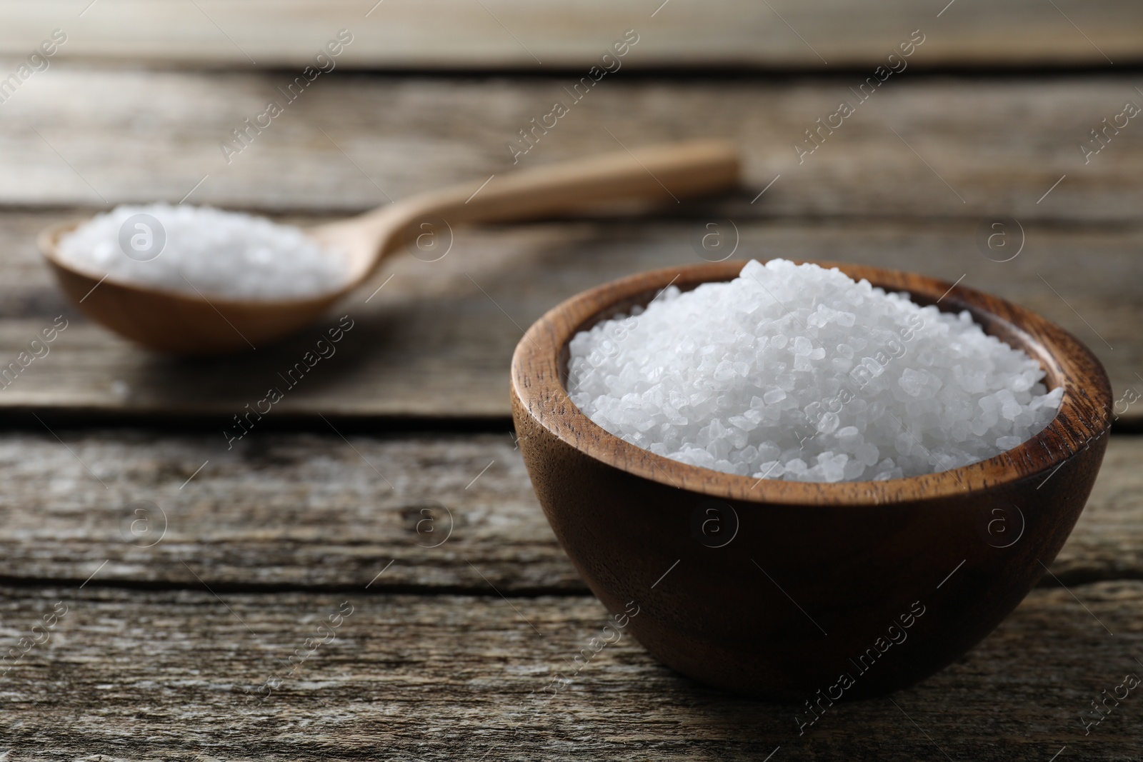 Photo of Organic salt in bowl and spoon on wooden table, closeup. Space for text