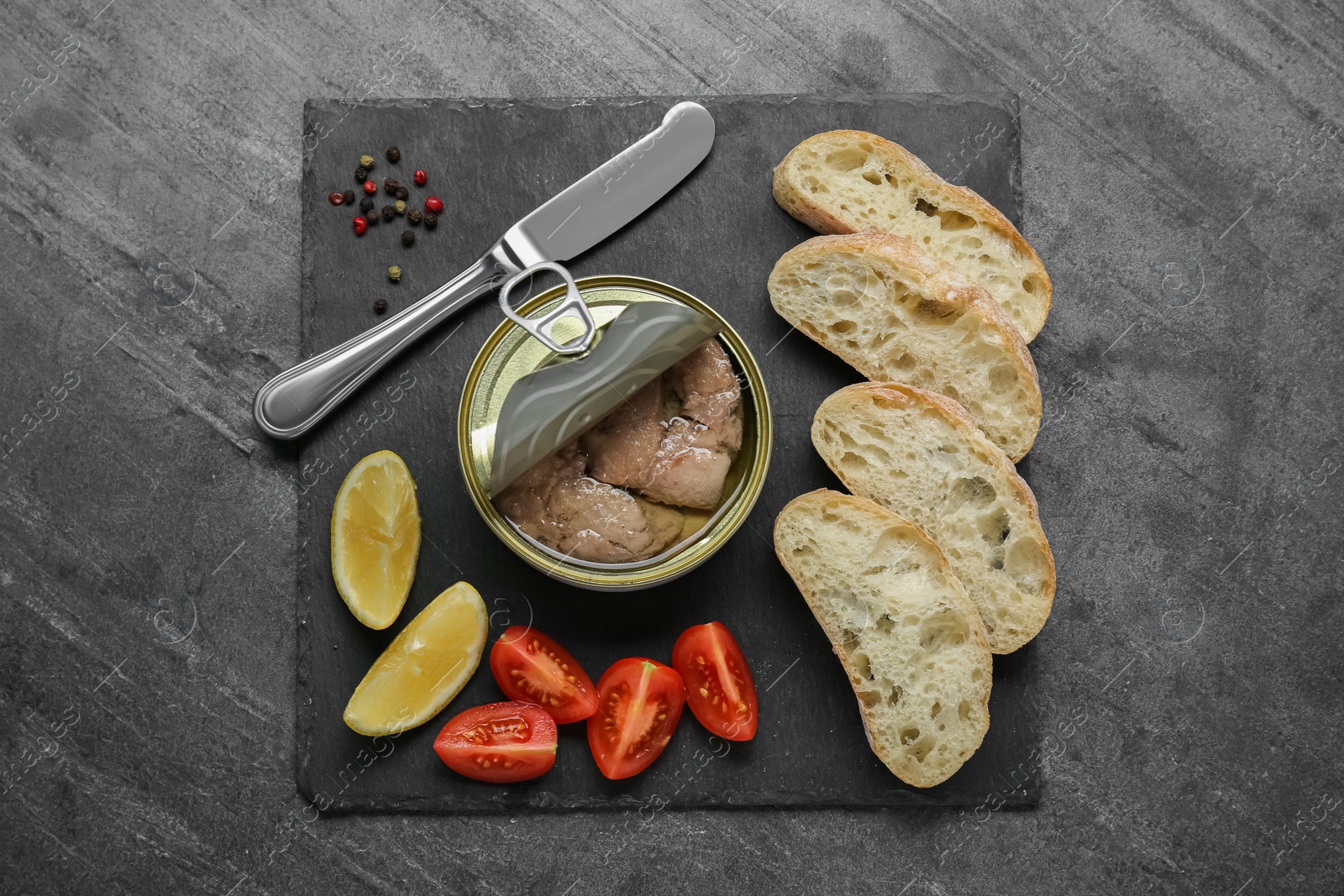 Photo of Flat lay composition with tin can of tasty cod liver and different products on black table