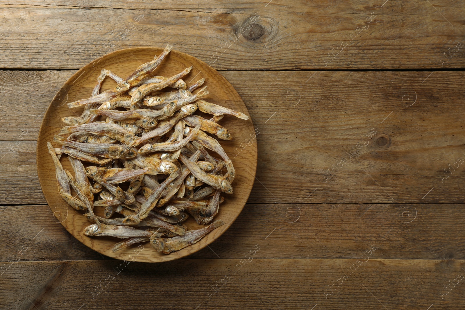 Photo of Delicious dried anchovies on wooden table, top view. Space for text