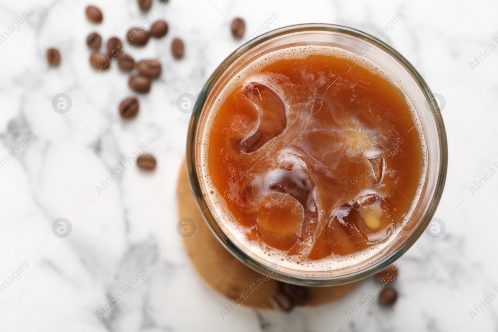 Photo of Refreshing iced coffee with milk in glass and beans on white marble table, top view. Space for text