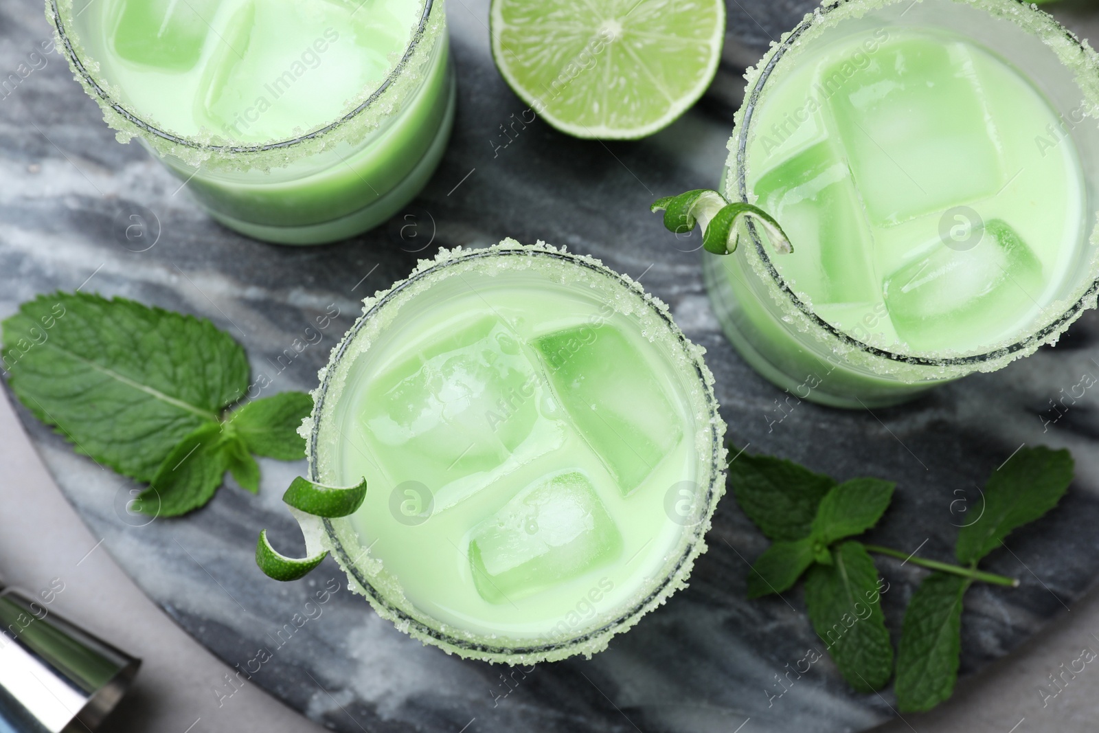 Photo of Delicious mint liqueur with ice cubes and green leaves on grey table, flat lay