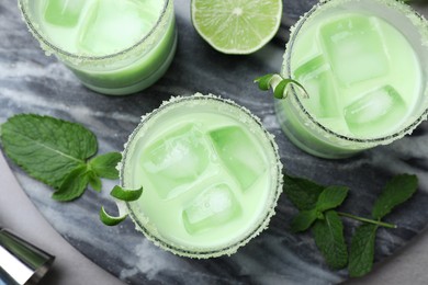 Photo of Delicious mint liqueur with ice cubes and green leaves on grey table, flat lay