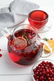 Photo of Tasty hot cranberry tea with lemon, rosemary and fresh berries in teapot on white wooden table