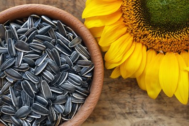 Photo of Bowl with organic sunflower seeds and flower on wooden table, flat lay