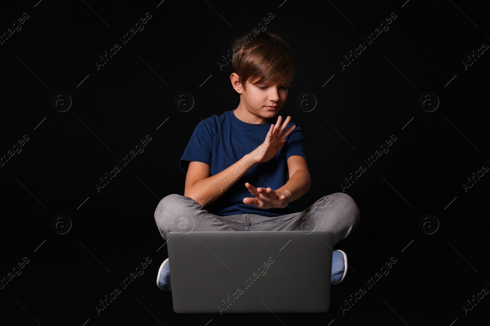 Photo of Scared child with laptop on black background. Danger of internet