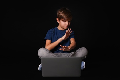 Photo of Scared child with laptop on black background. Danger of internet