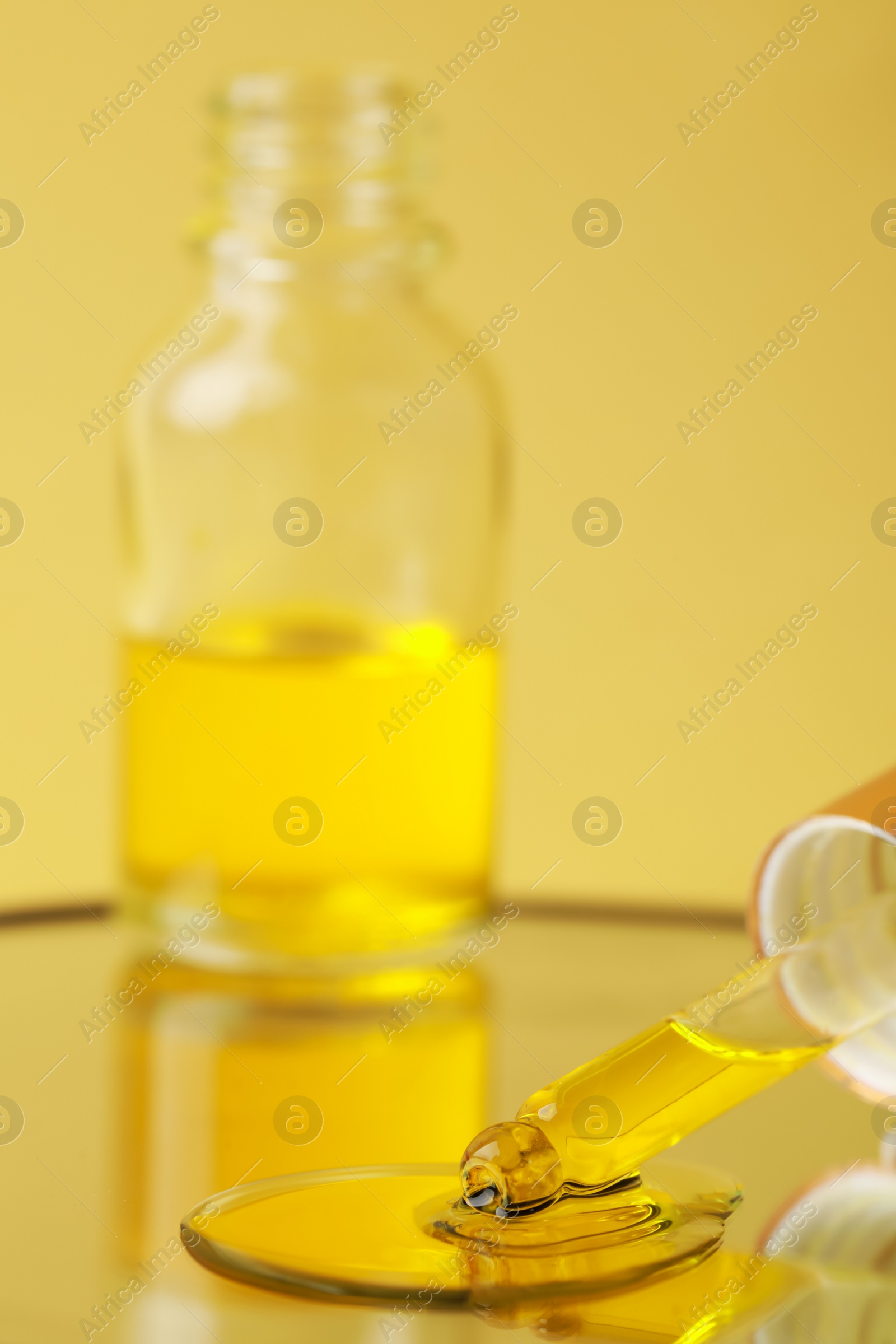 Photo of Dripping face serum from pipette on mirror against yellow background