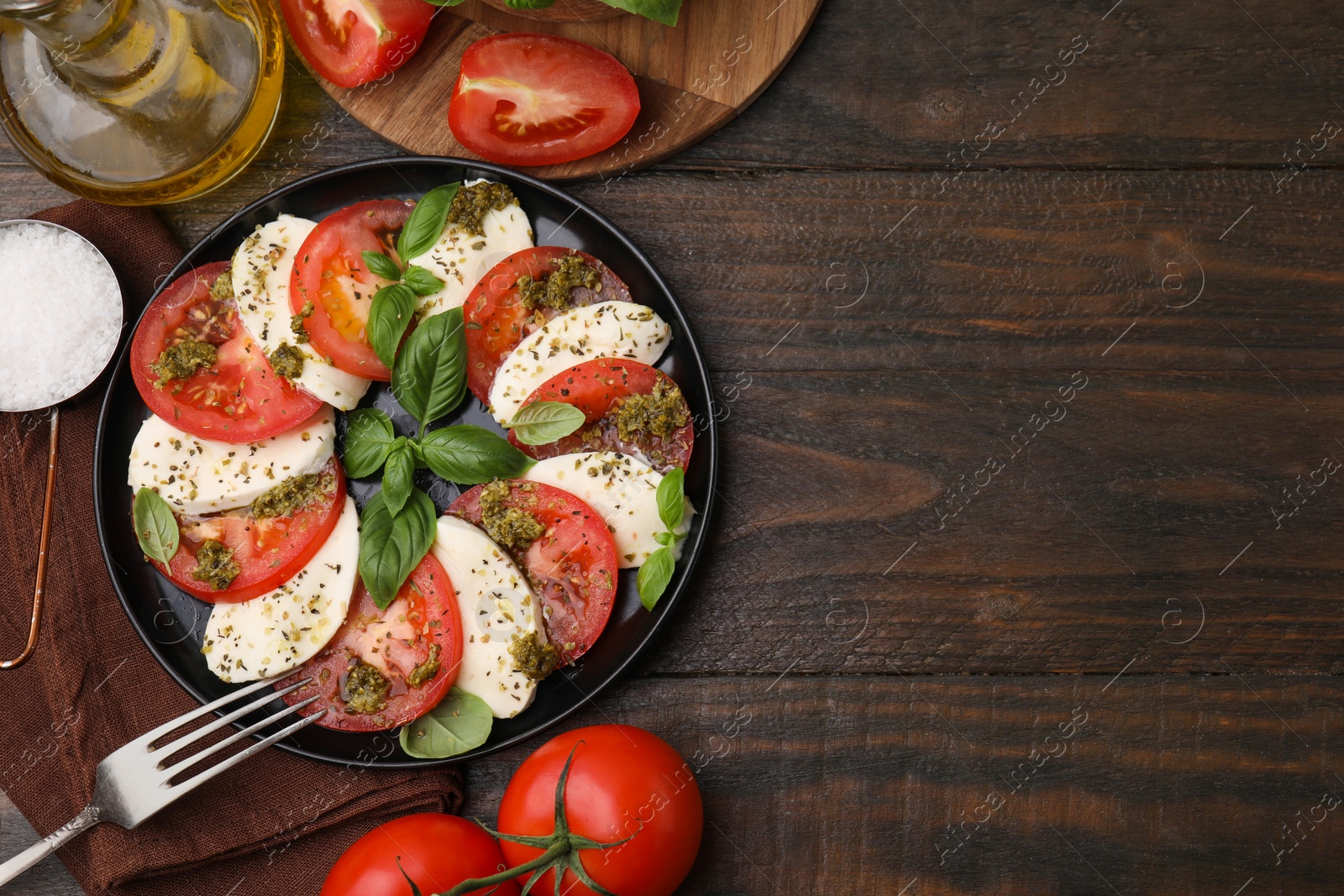 Photo of Plate of delicious Caprese salad with pesto sauce, fork and ingredients on wooden table, flat lay. Space for text