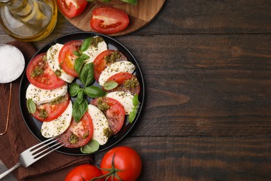 Plate of delicious Caprese salad with pesto sauce, fork and ingredients on wooden table, flat lay. Space for text