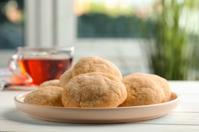 Photo of Delicious sugar cookies and cup of tea on white wooden table, closeup