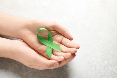 Photo of Woman holding green ribbon on grey background. Cancer awareness