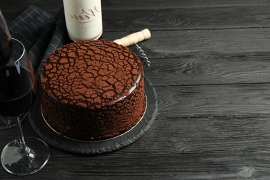 Photo of Delicious chocolate truffle cake, red wine and corkscrew on black wooden table, space for text