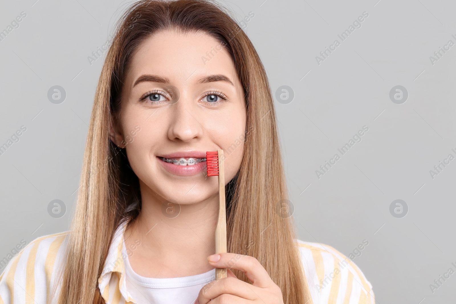 Photo of Portrait of smiling woman with dental braces and toothbrush on grey background
