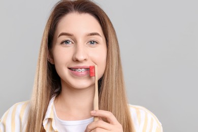 Portrait of smiling woman with dental braces and toothbrush on grey background