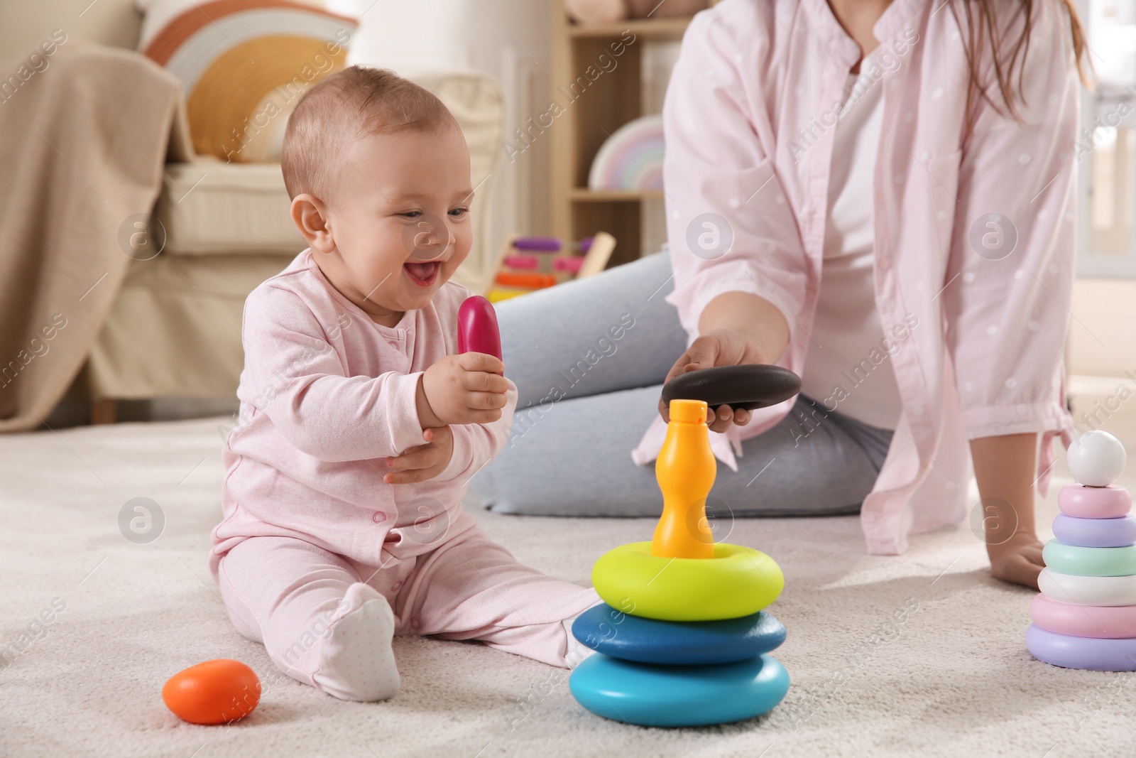 Photo of Cute baby girl and mother playing with toy pyramid on floor at home