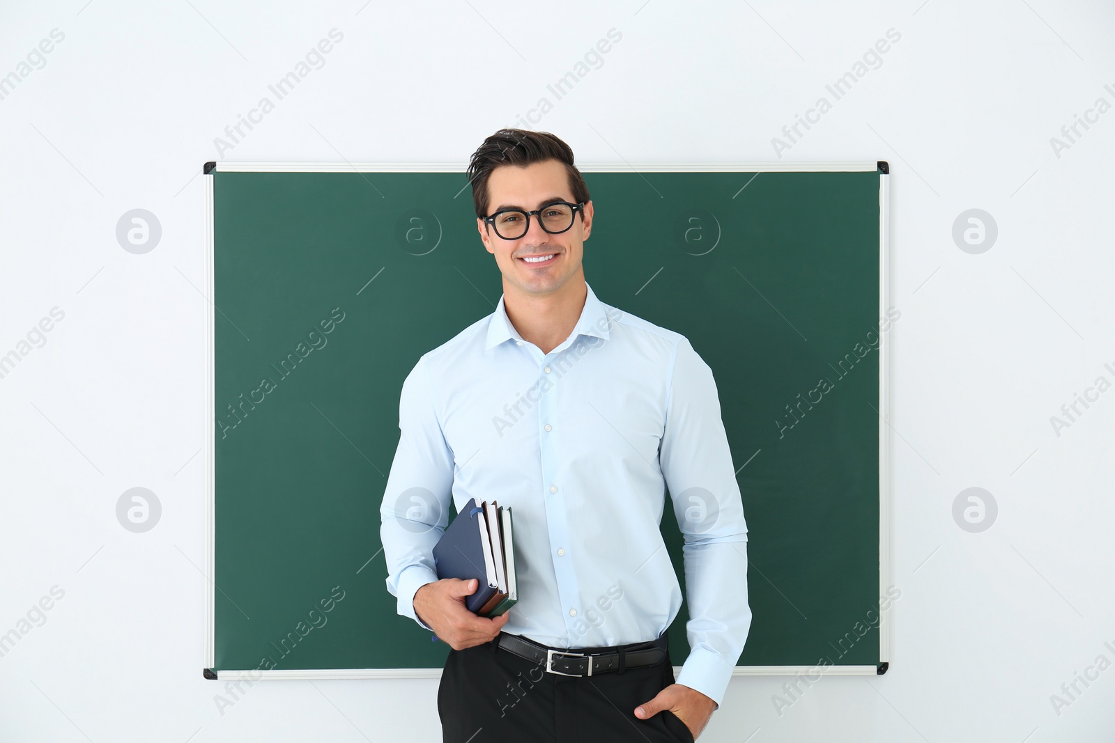 Photo of Young teacher with book near blank chalkboard in classroom