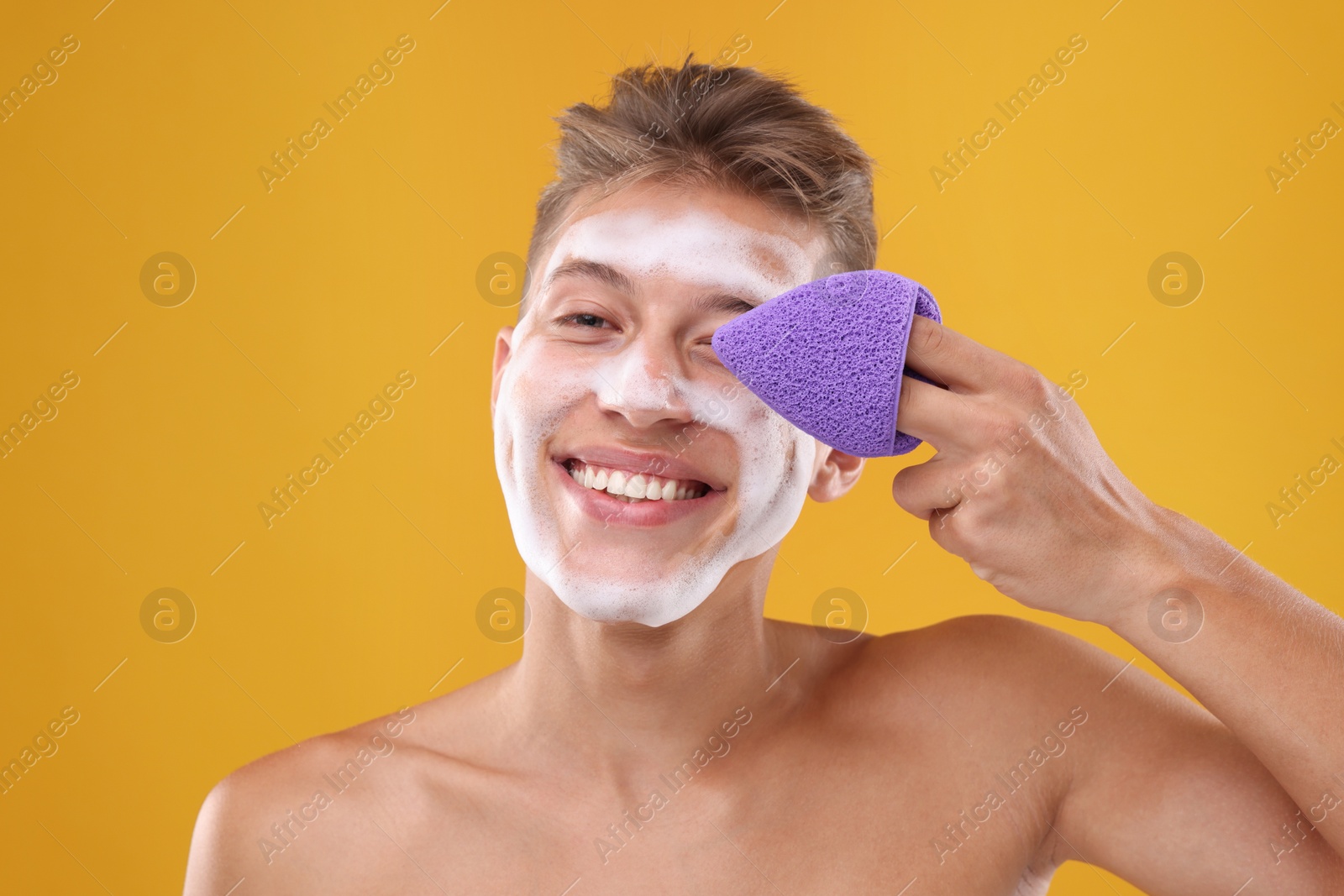 Photo of Happy young man washing his face with sponge on orange background