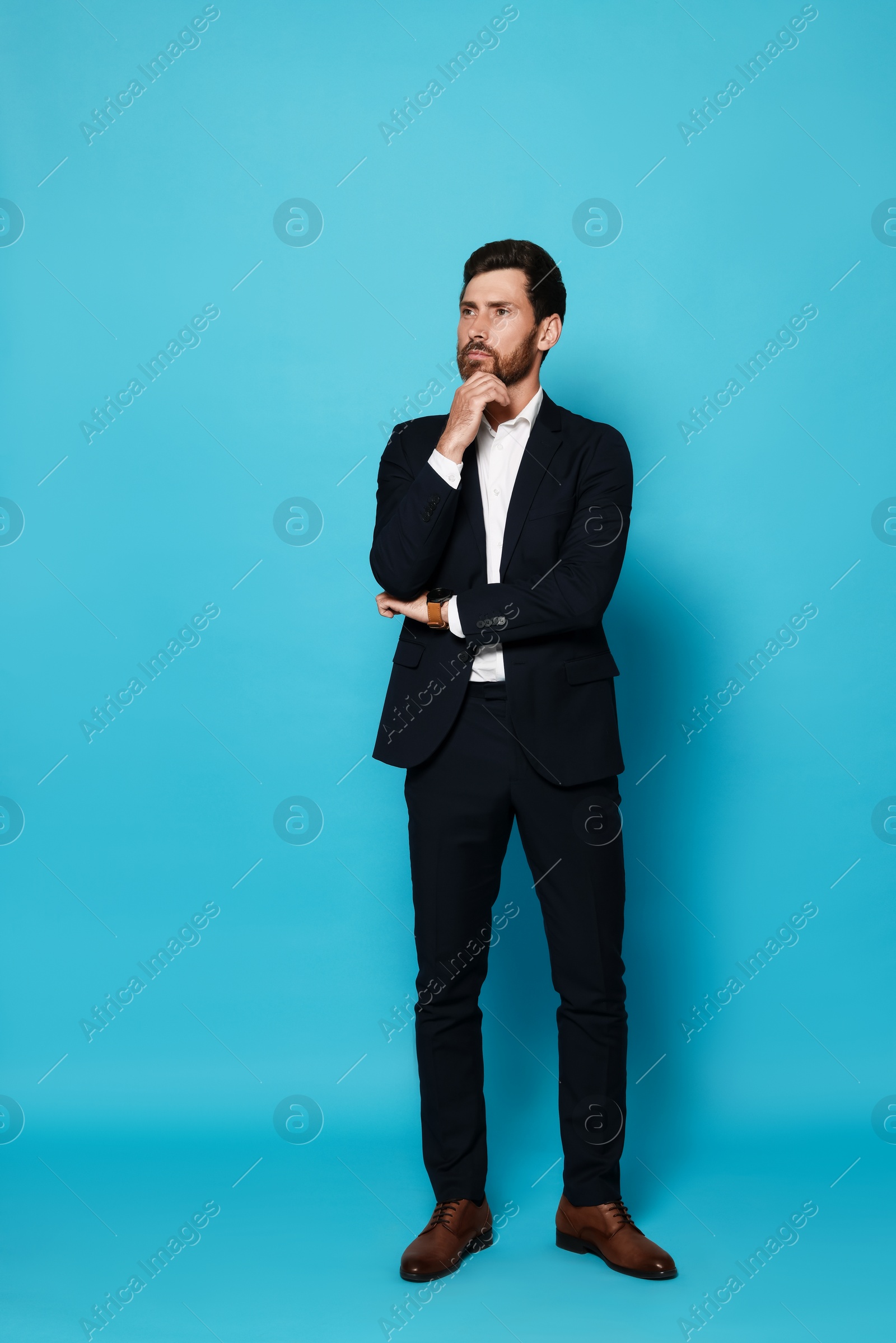 Photo of Pensive bearded man in suit looking away on light blue background