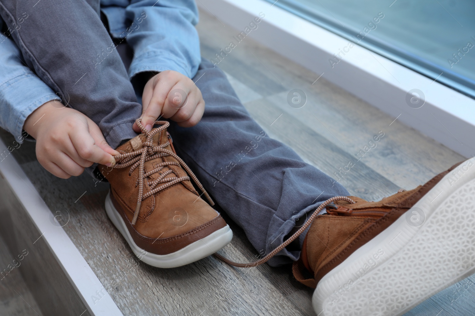 Photo of Little boy tying shoe laces at home, closeup