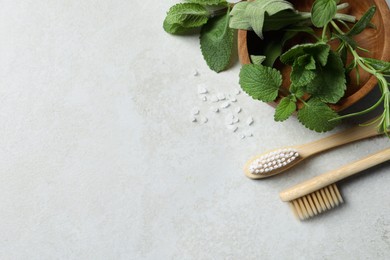 Photo of Toothbrushes, sea salt and green herbs on light grey table, flat lay. Space for text