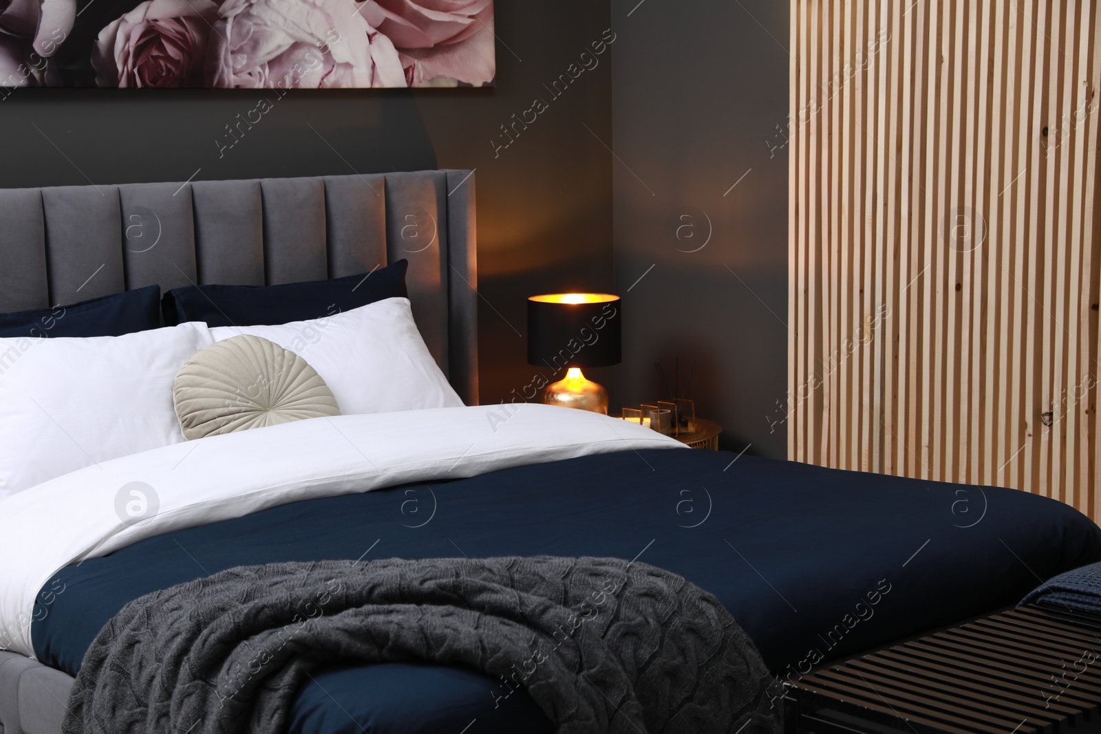 Photo of Lamp, ottoman and comfortable bed with cushions in room. Stylish interior