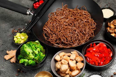 Wok with noodles, chicken and other products on grey table