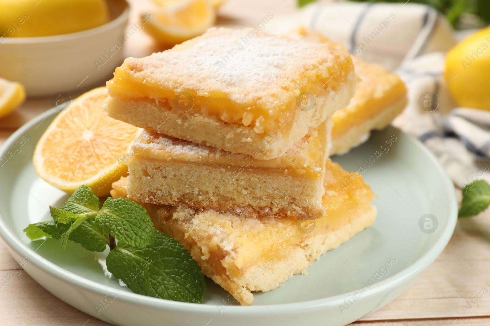 Photo of Tasty lemon bars with powdered sugar and mint on table, closeup