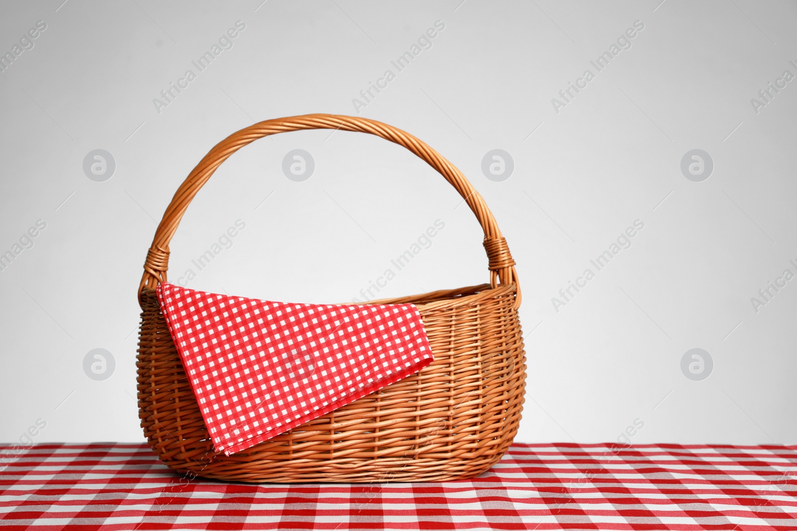 Photo of Wicker picnic basket with napkin on checkered tablecloth against white background