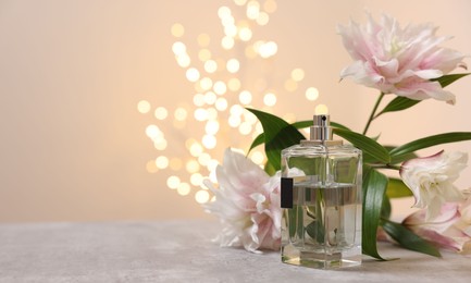 Bottle of perfume and beautiful lily flowers on table against beige background with blurred lights, space for text