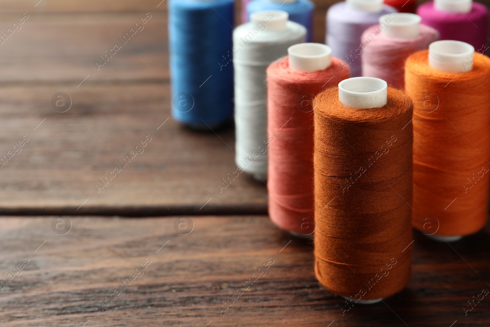 Photo of Different colorful sewing threads on wooden table, closeup. Space for text