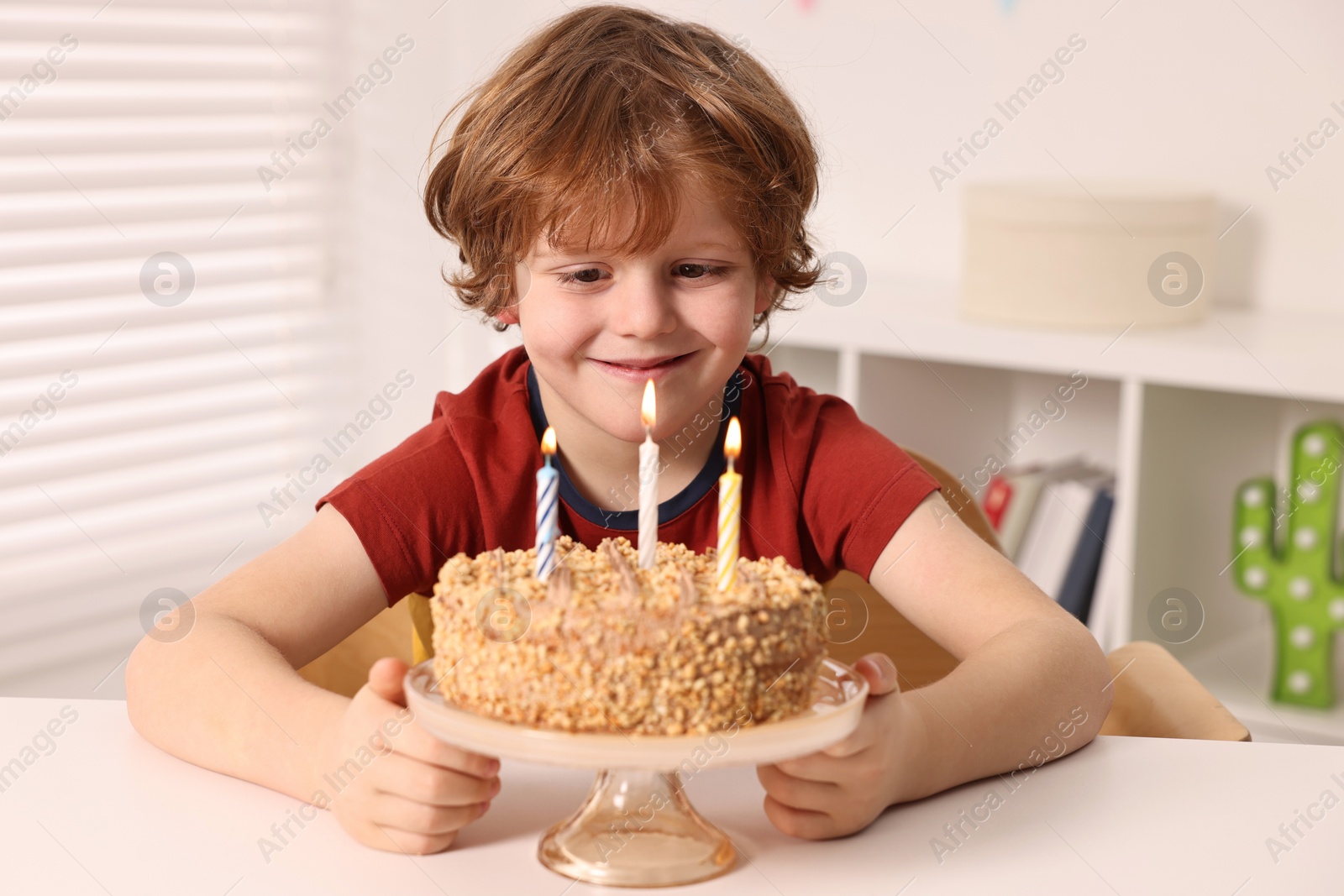 Photo of Cute boy with birthday cake at table indoors