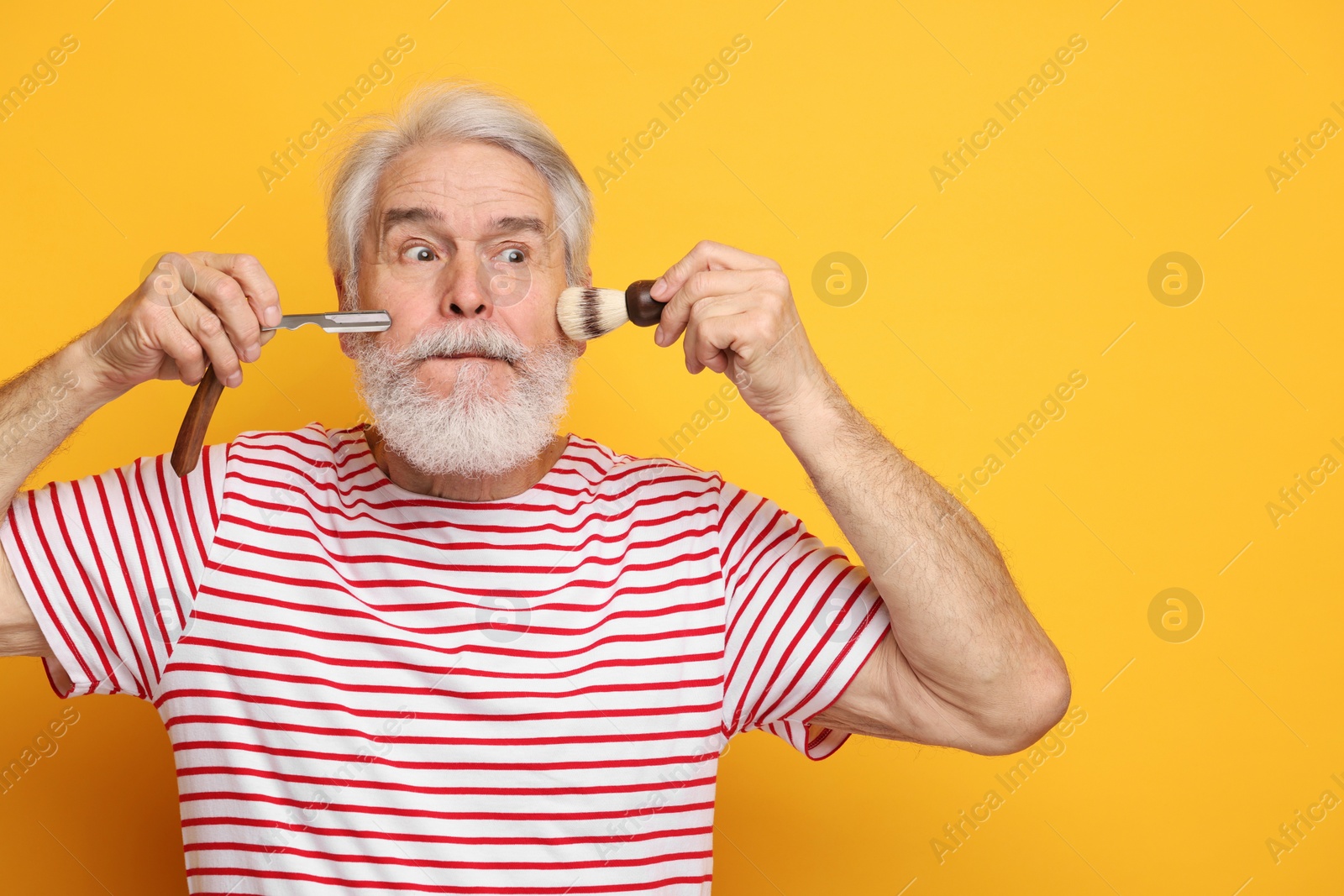 Photo of Senior man with mustache holding blade and brush on orange background