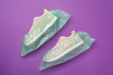 Photo of Sneakers in shoe covers on purple background, top view