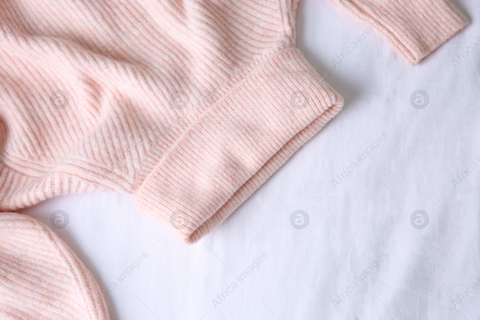 Photo of Pink warm sweater on white crumpled fabric, top view