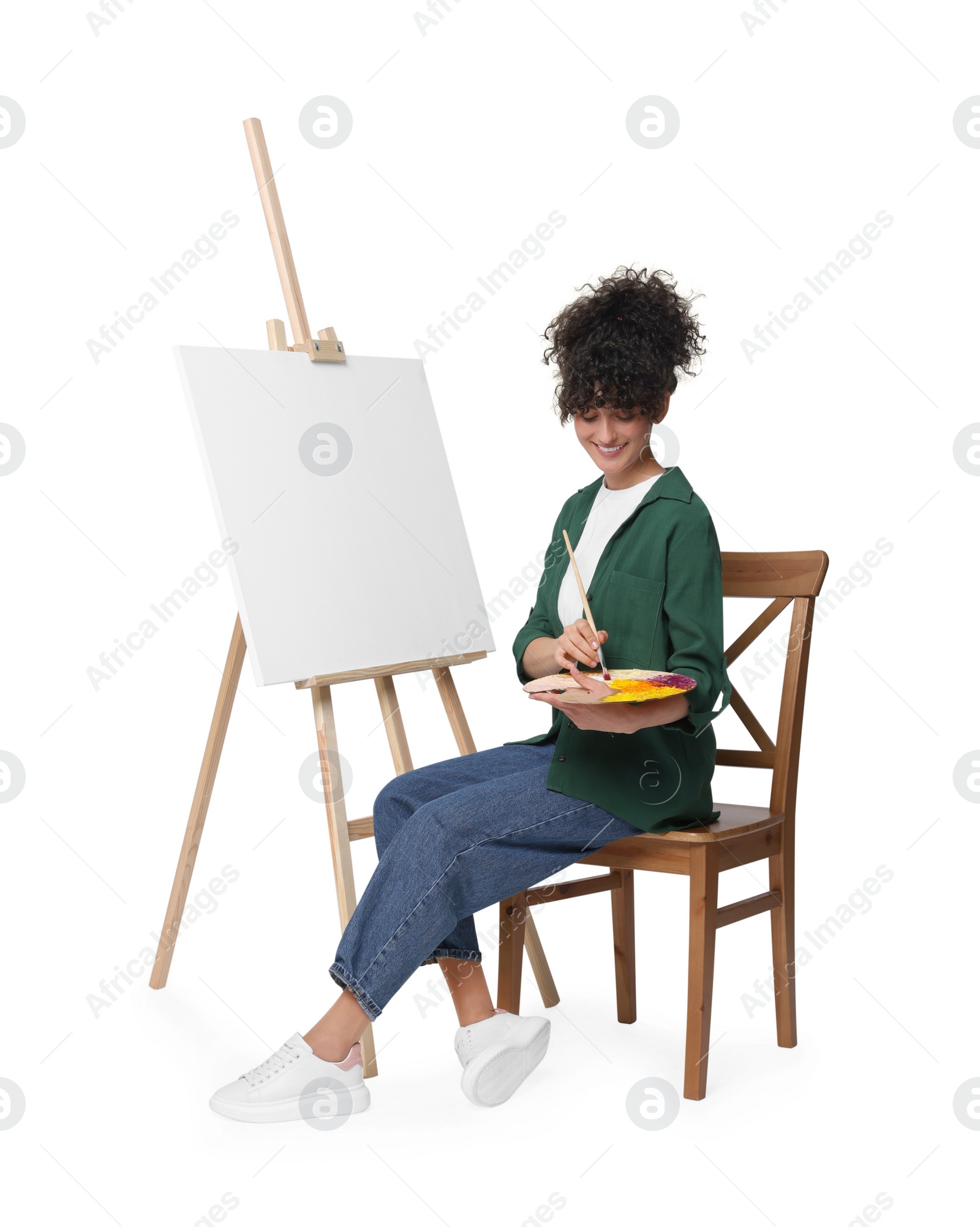 Photo of Young woman painting on easel with canvas against white background