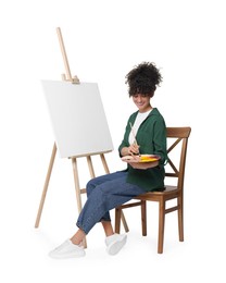 Young woman painting on easel with canvas against white background