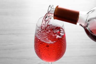 Pouring delicious rose wine into glass on white table, closeup