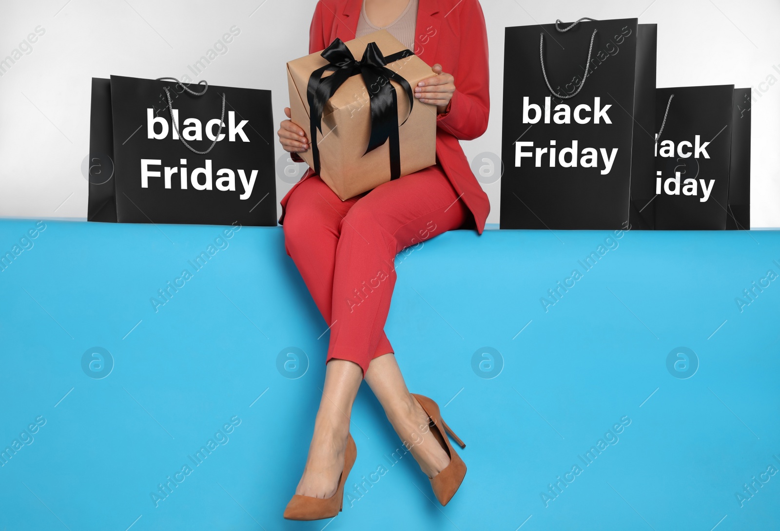 Photo of Woman with gift box and shopping bags sitting on light blue background, closeup. Black Friday