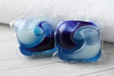 Laundry capsules and towel on white wooden table, closeup