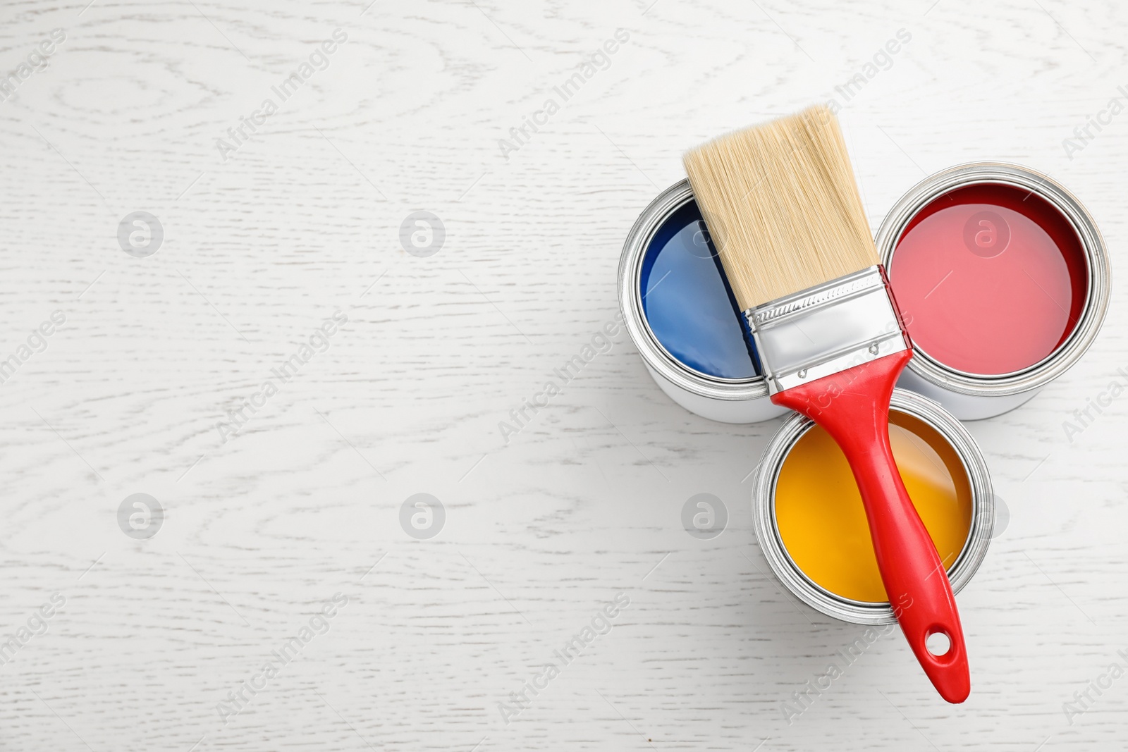 Photo of Open cans with paint and brush on white wooden table, flat lay. Space for text