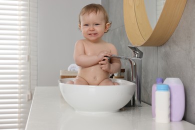 Cute little baby bathing in sink indoors