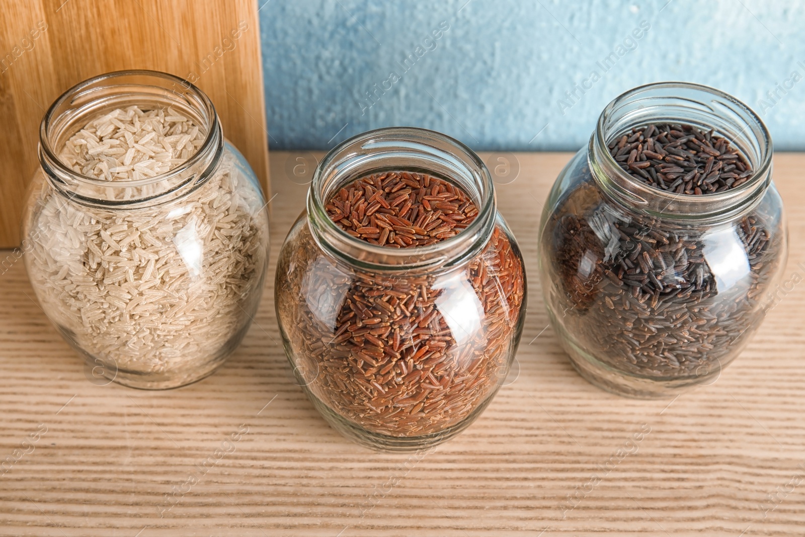 Photo of Jars with different types of rice on wooden table