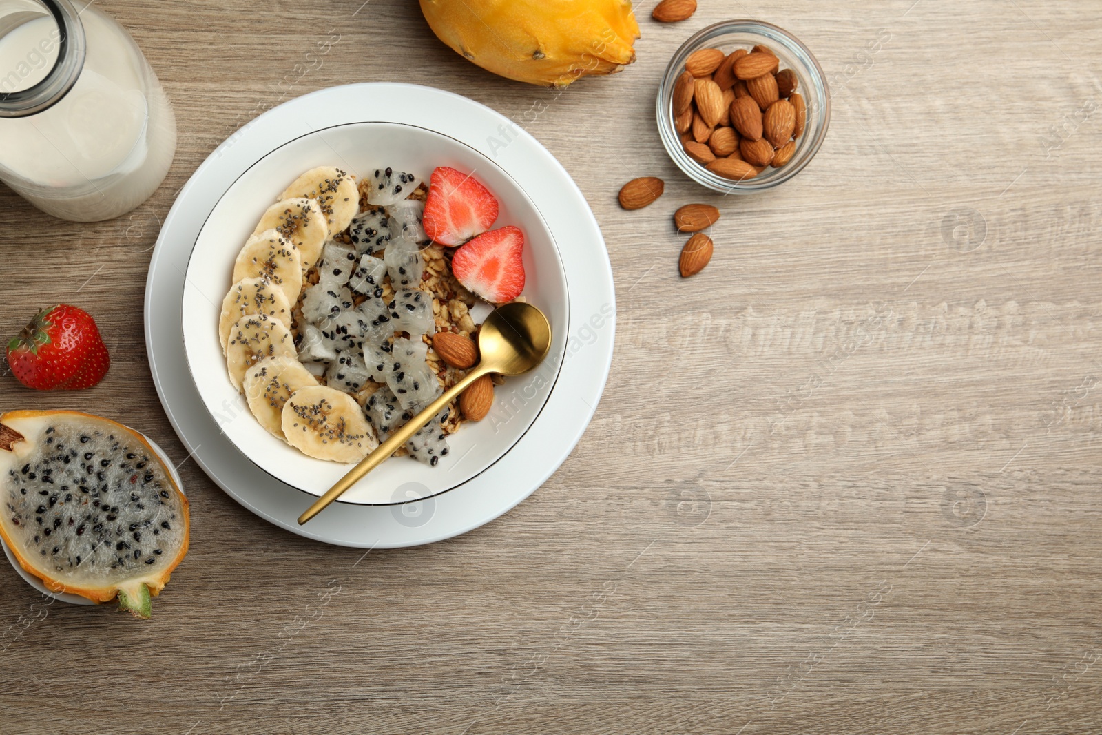 Photo of Bowl of granola with pitahaya, banana, almond and strawberry on wooden table, flat lay. Space for text