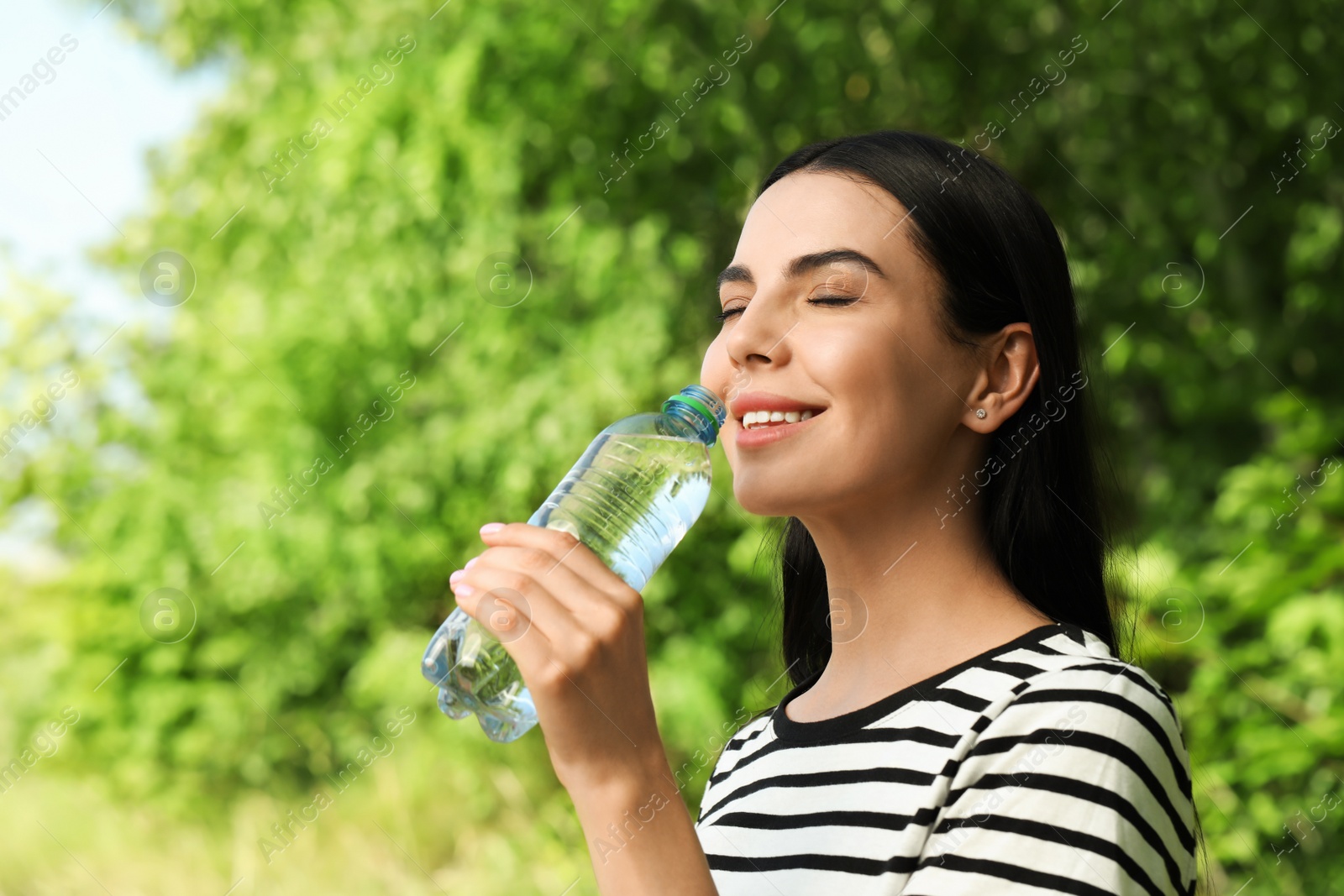 Photo of Young woman drinking water outdoors. Refreshing drink