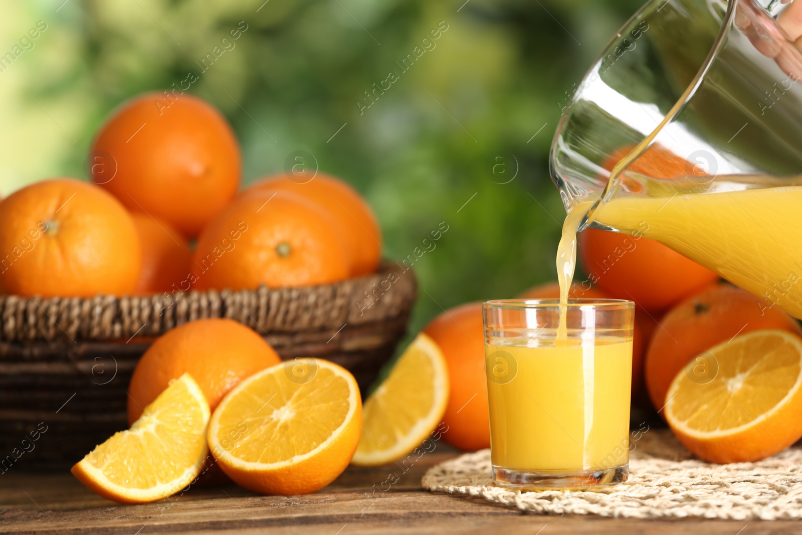 Photo of Pouring delicious orange juice into glass at wooden table against blurred background, closeup